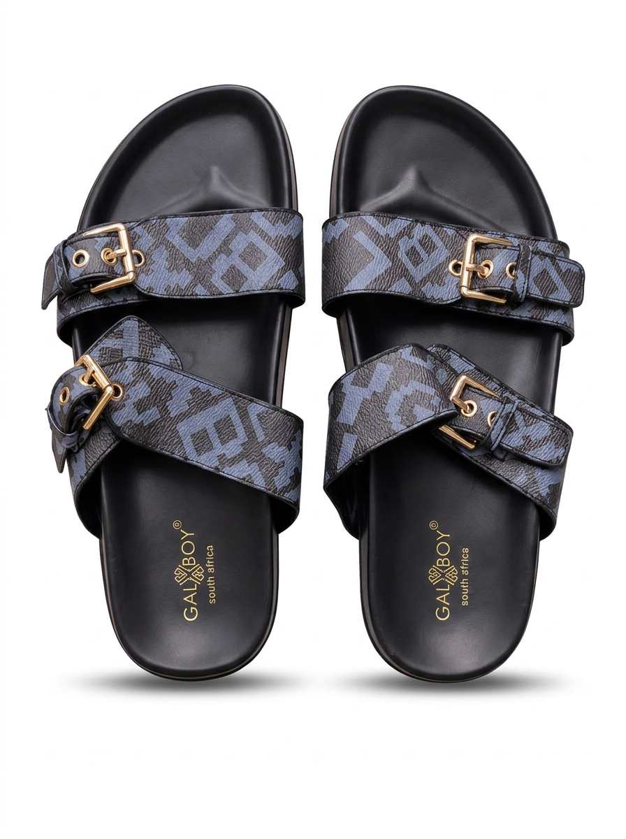 Pair of grey monogram print double-buckle slide sandals with gold buckles and black footbeds on a plain white background