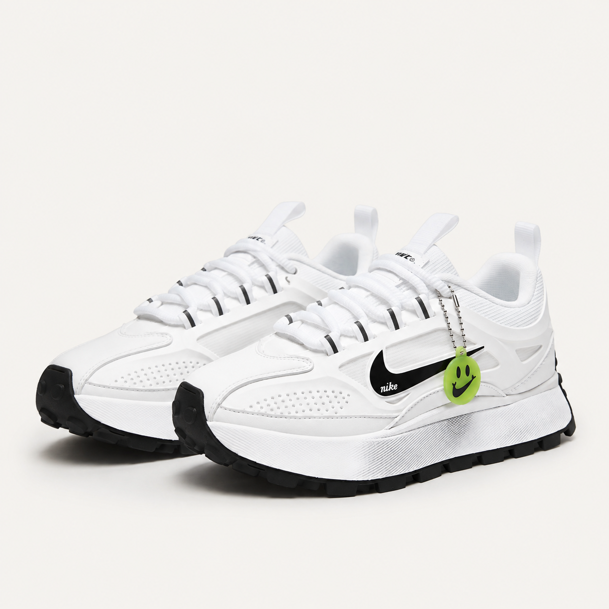 Nike Waffle sneakers in white and black with green smiley charm on the laces, angled pair view
