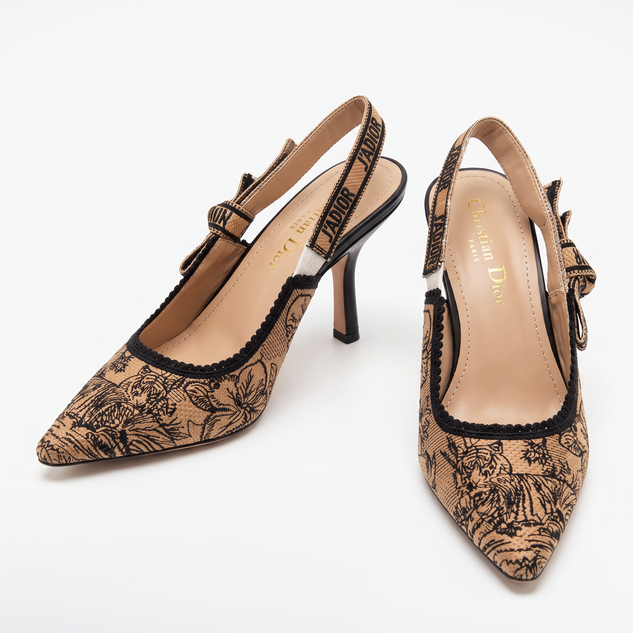 Pair of beige Dior J'adior slingback pumps in embroidered toile de Jouy fabric with black ribbon straps on a plain white background